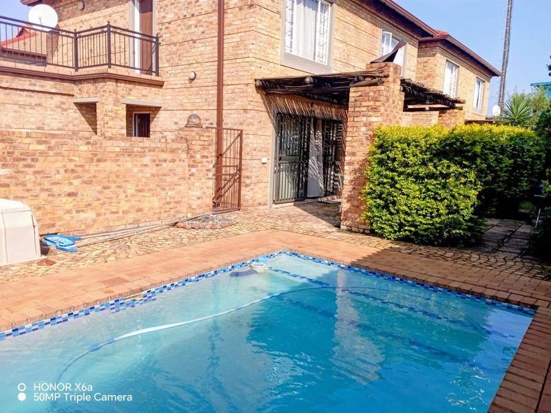 Rear exterior view of a brick townhouse featuring a swimming pool, paved patio area, and a covered pergola.