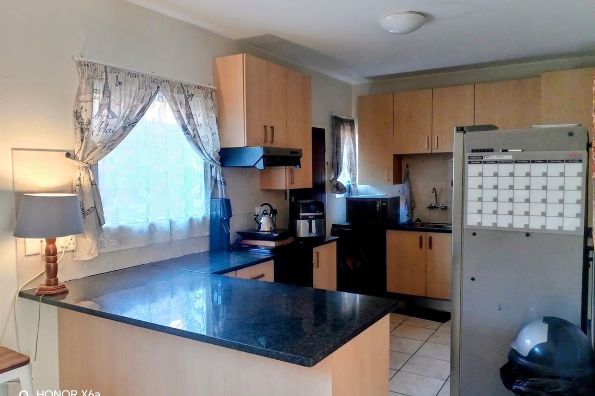 A functional kitchen featuring light wood-finish cabinetry, dark granite countertops, and tiled flooring, providing a practical workspace with integrated storage and preparation areas.