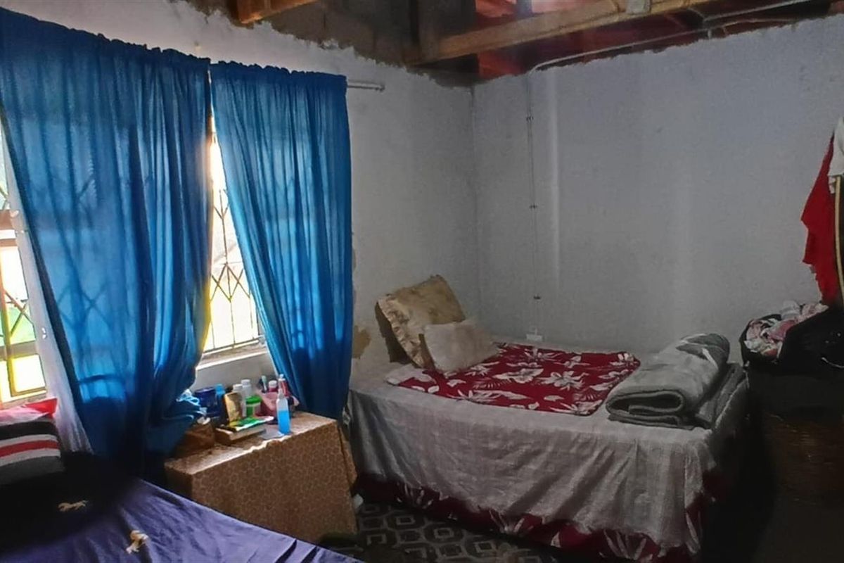 A bedroom featuring security bars on the window, currently requiring significant finishing work on the walls and ceiling to complete the space.