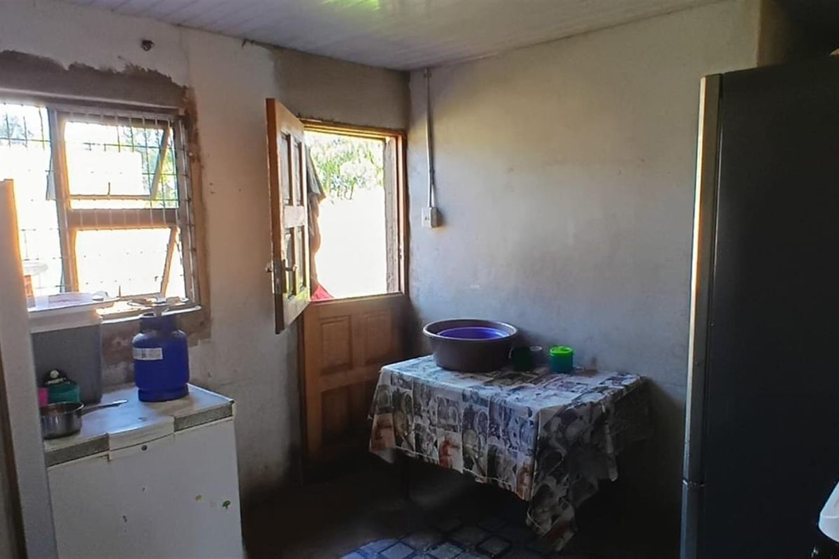 A basic kitchen area featuring a timber door and window with security bars, currently requiring significant renovation and finishing of wall surfaces.