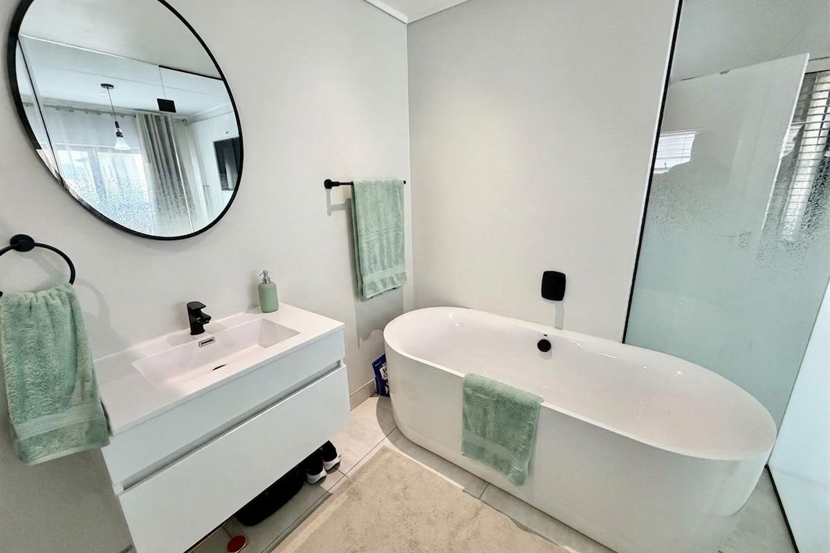 Modern bathroom featuring a sleek wall-mounted vanity with a black faucet, a contemporary freestanding bathtub, and a circular mirror.