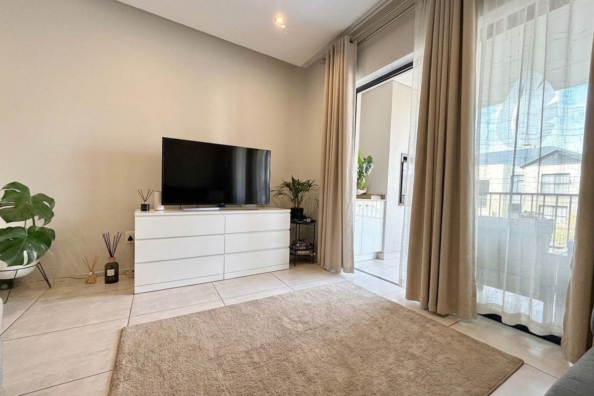 A bright living room featuring large sliding glass doors that open onto a private balcony, finished with neutral floor tiles and recessed lighting.