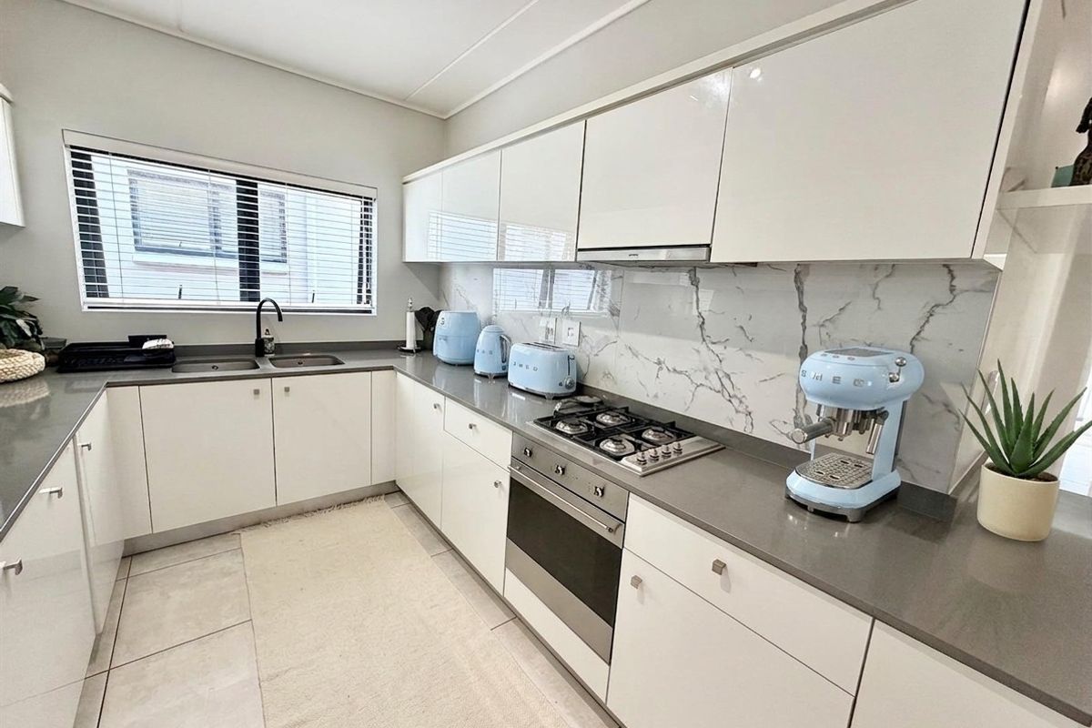 Modern kitchen featuring white cabinetry, stone countertops, marble-look splashback, built-in gas hob, and stainless steel oven.