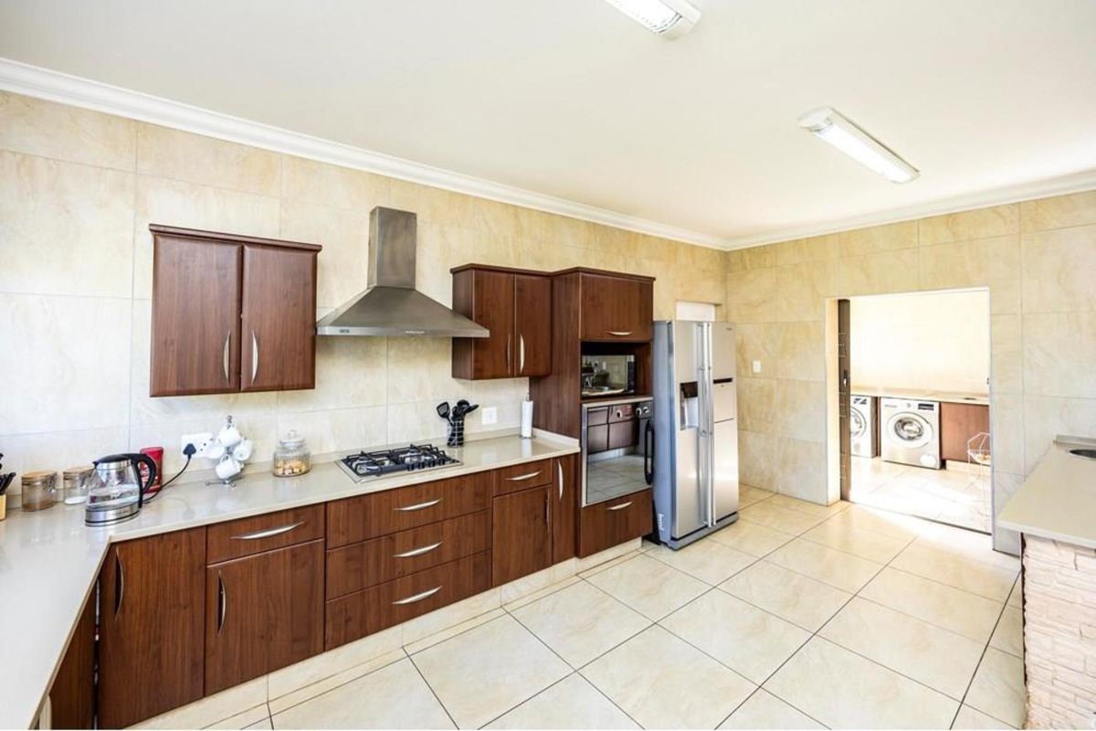A well-maintained kitchen featuring dark wood cabinetry, stone countertops, a gas hob with extractor fan, and tiled finishes, with an adjacent laundry area.
