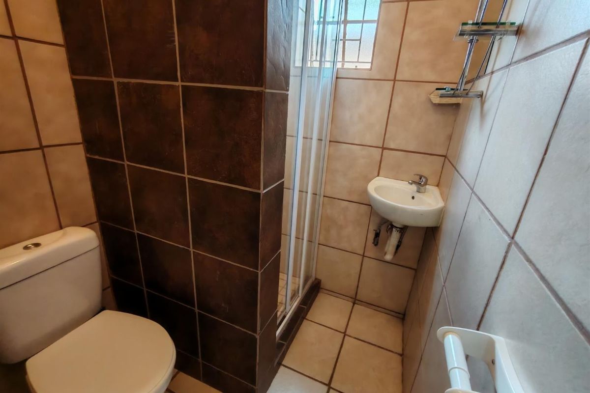 Compact bathroom featuring a corner basin, a tiled shower enclosure, and a standard toilet with floor-to-ceiling wall tiling.