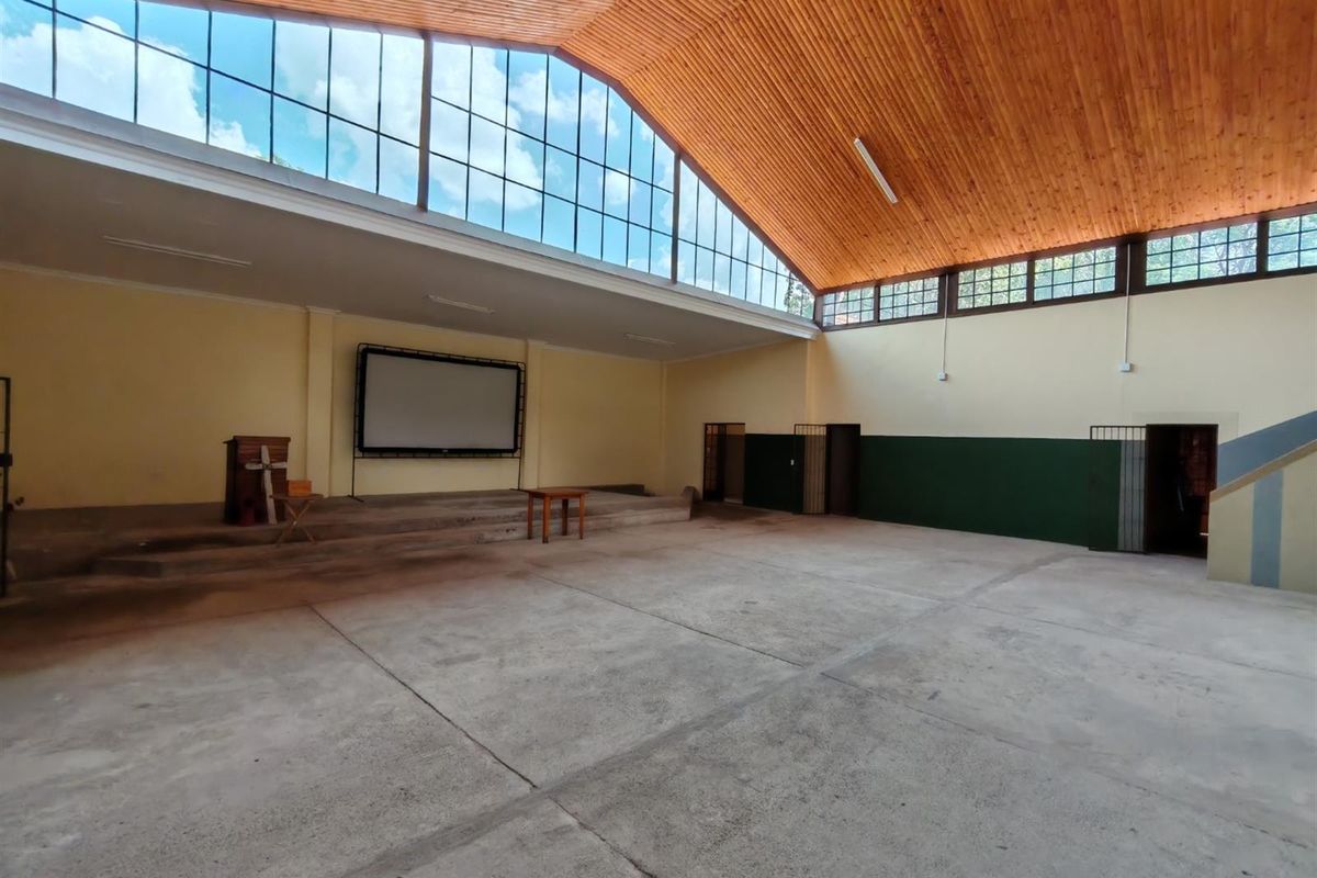 Spacious commercial hall featuring a high vaulted timber ceiling, large clerestory windows, a raised stage area, and durable concrete flooring.