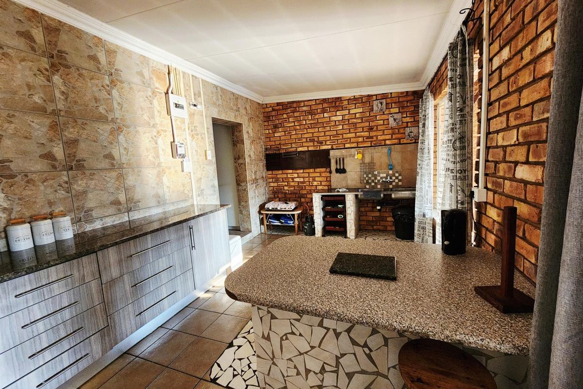 A rustic kitchen featuring exposed brick walls, stone-tiled feature wall, granite countertops, and a central island with a mosaic-tiled base.