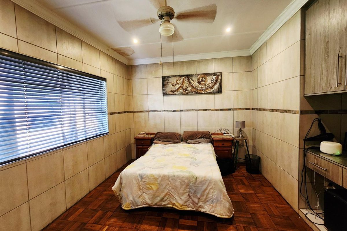 A bedroom featuring parquet flooring and full-height wall tiling, equipped with a ceiling fan and built-in cabinetry.