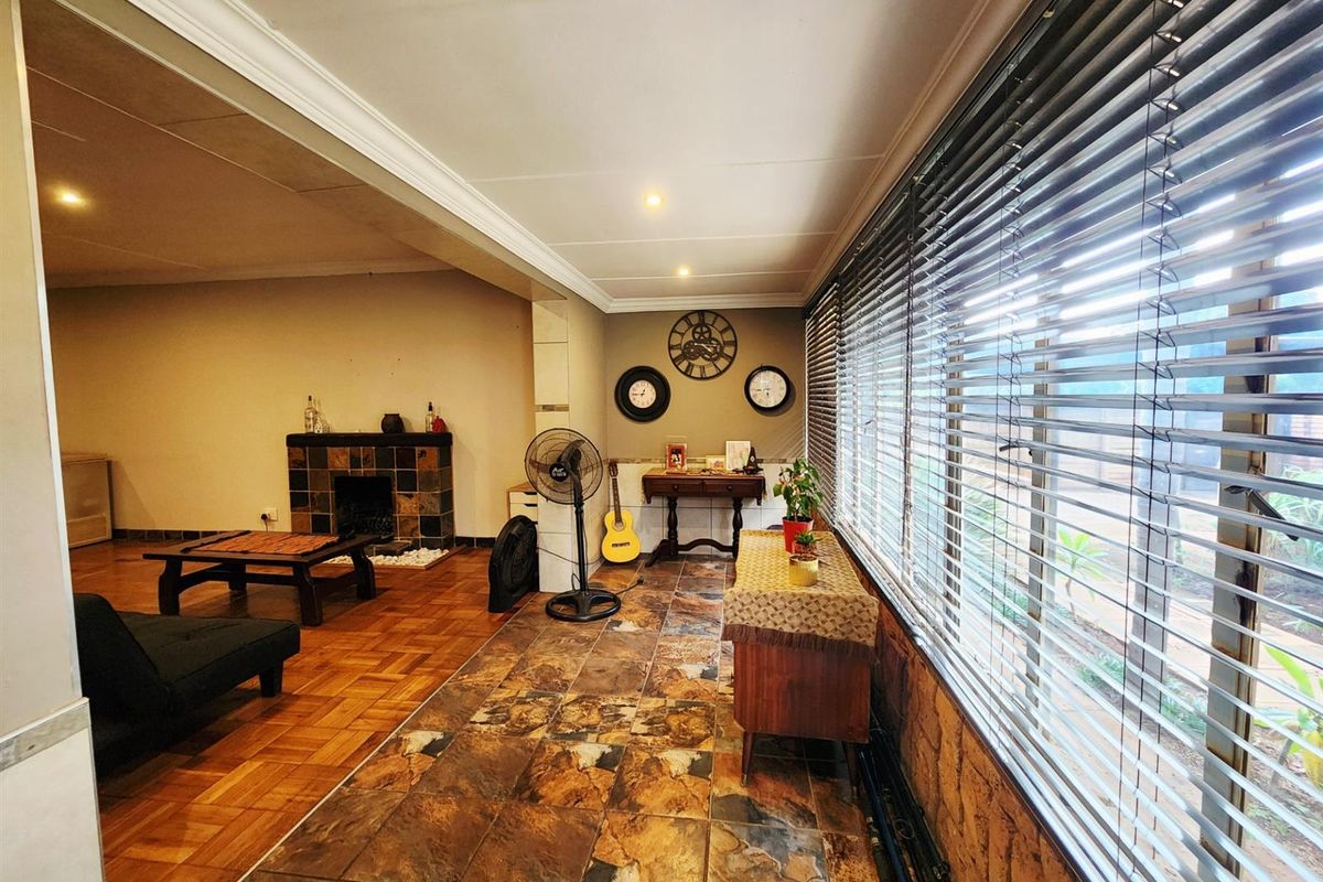 Spacious living area featuring a tiled floor, a built-in fireplace with stone cladding, and large windows with venetian blinds.