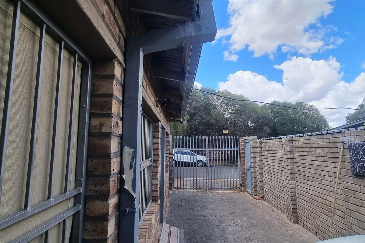 Side exterior walkway featuring brick wall construction, security gates, and paved pathway leading towards the street entrance.
