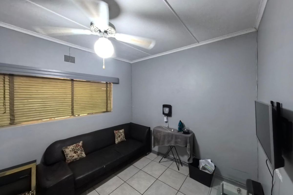 A living room featuring tiled flooring, a ceiling fan, and a window with fitted blinds.
