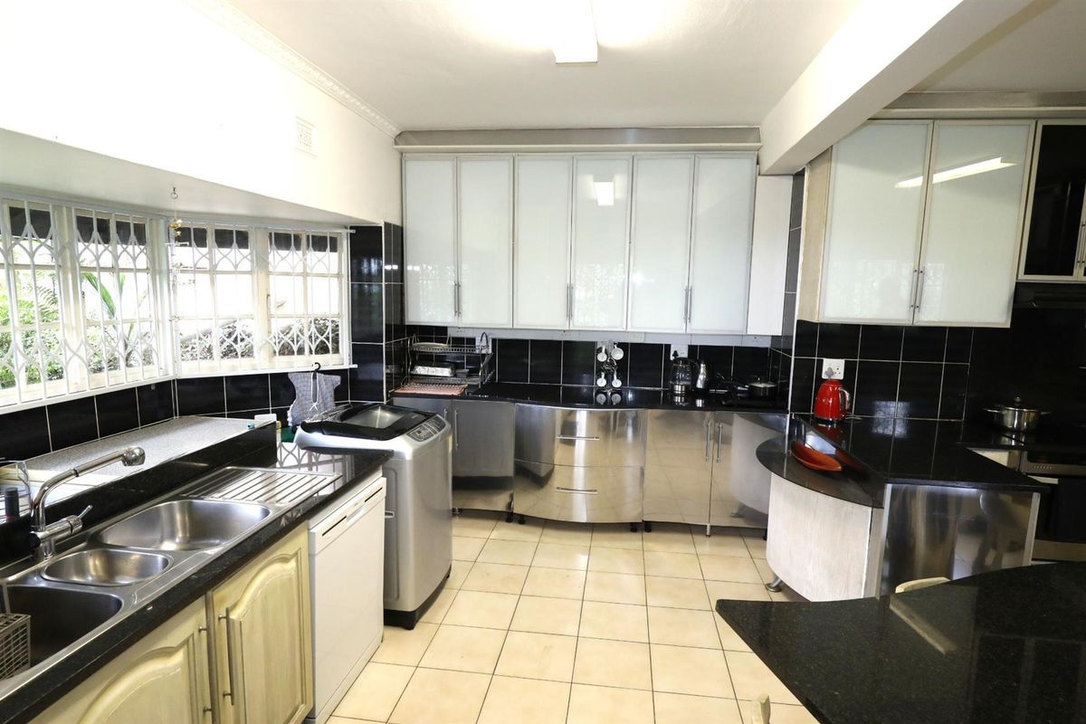 A functional kitchen featuring stainless steel and white cabinetry, black granite countertops, double basin sink, and tiled flooring with ample natural light.