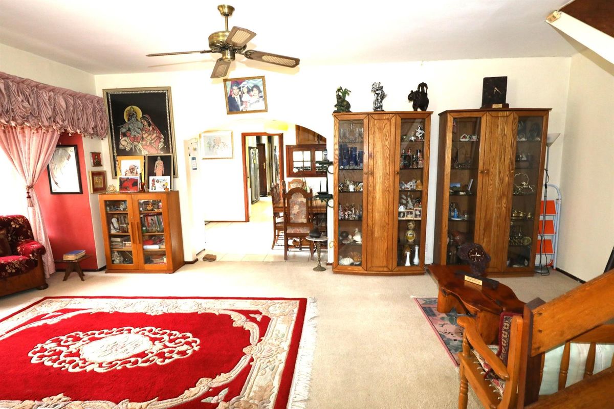 A spacious living room featuring a ceiling fan, carpeted flooring, and an arched entryway leading to the dining area.