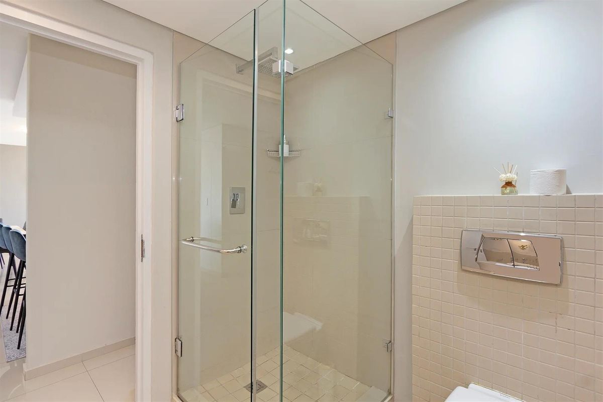 Modern bathroom featuring a glass-enclosed shower with wall-mounted fixtures and a wall-mounted flush plate for the concealed cistern.