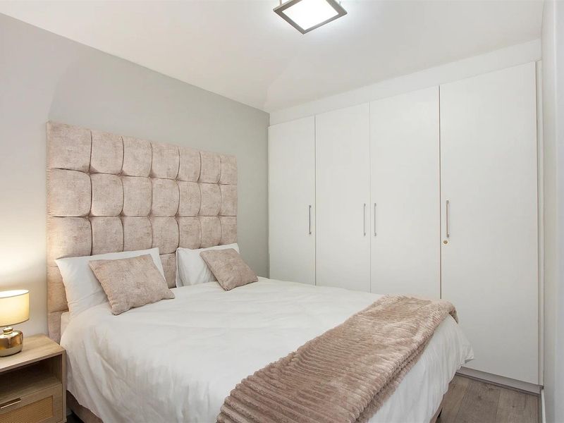 A well-maintained bedroom featuring neutral tones, laminate flooring, and ample storage with a large built-in wardrobe.