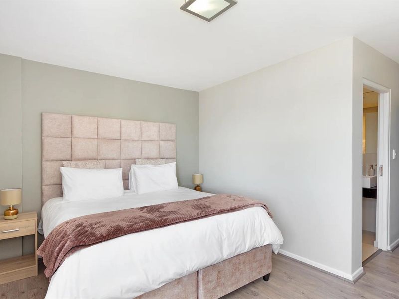 A well-maintained bedroom featuring neutral wall tones, laminate flooring, and direct access to an en-suite bathroom.