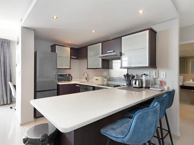 Modern kitchen featuring dark cabinetry, quartz countertops, a breakfast bar, and recessed lighting, seamlessly integrated into an open-plan living space.