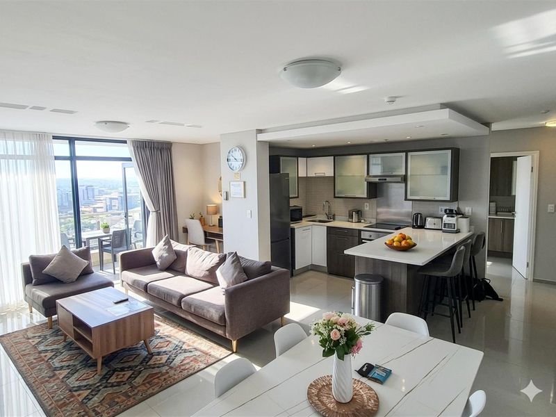 Modern open-plan apartment featuring a sleek kitchen with stone countertops, breakfast bar, and seamless flow to the living area and balcony with city views.