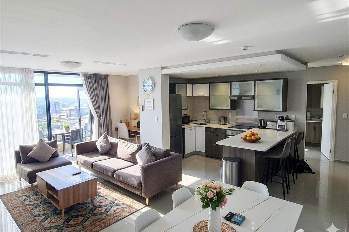 Modern open-plan apartment featuring a sleek kitchen with stone countertops, breakfast bar, and seamless flow to the living area and balcony with city views.