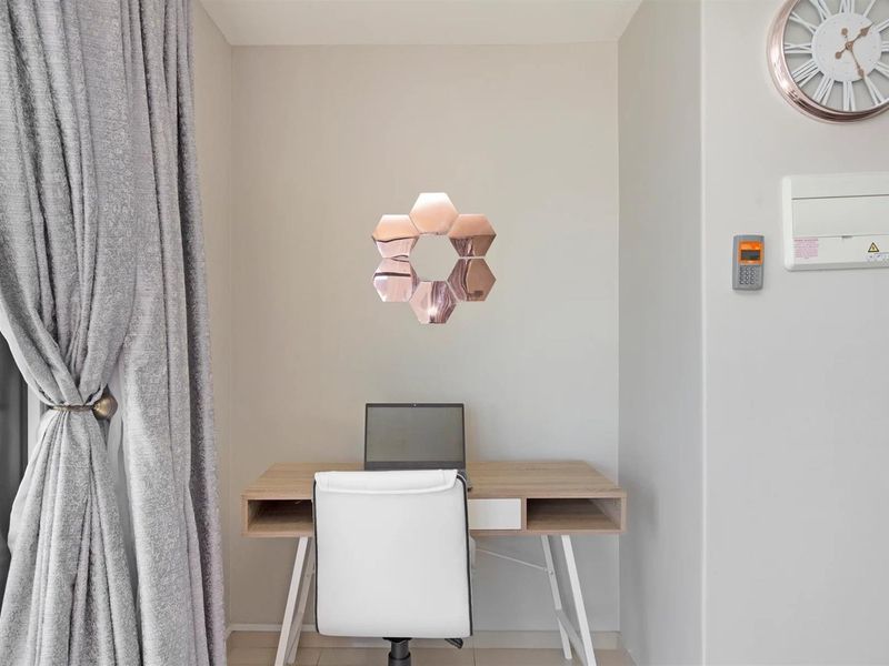 A compact home office nook featuring neutral wall finishes, integrated alarm and intercom systems, and natural light from the adjacent window.