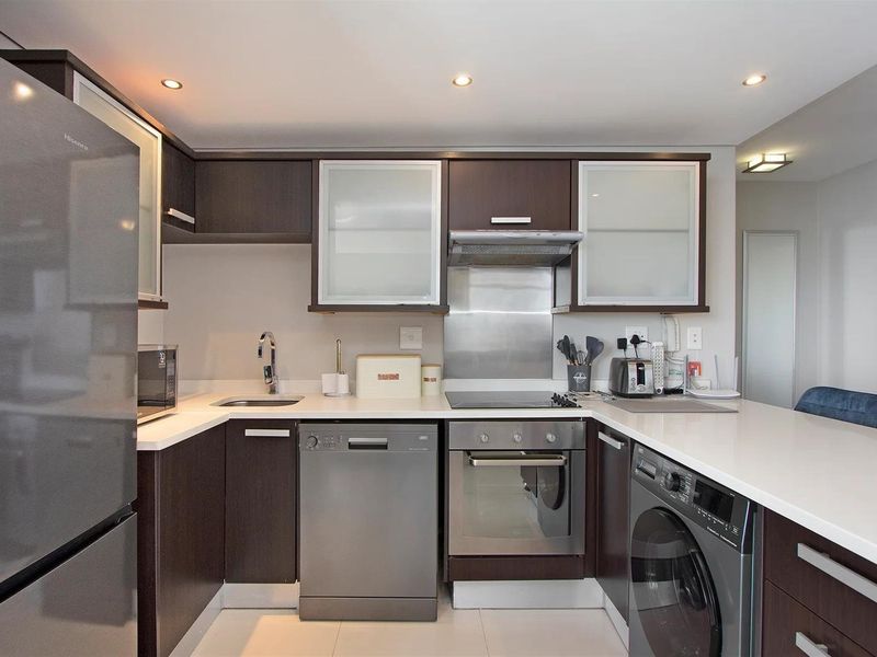 Modern kitchen featuring dark wood cabinetry, stone countertops, integrated stainless steel appliances, and recessed lighting in a clean, functional layout.