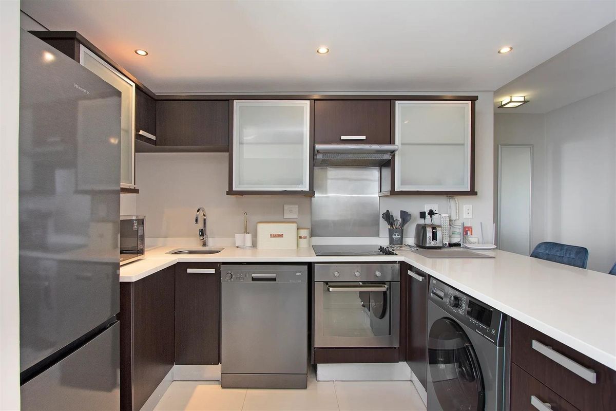 Modern kitchen featuring dark wood cabinetry, stone countertops, integrated stainless steel appliances, and recessed lighting in a clean, functional layout.