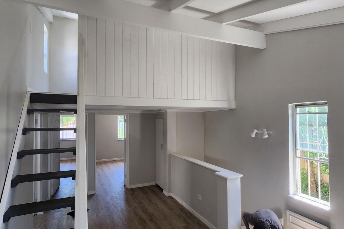 An interior view of a townhouse featuring a mezzanine level, wooden flooring, and a staircase leading to an upper area.