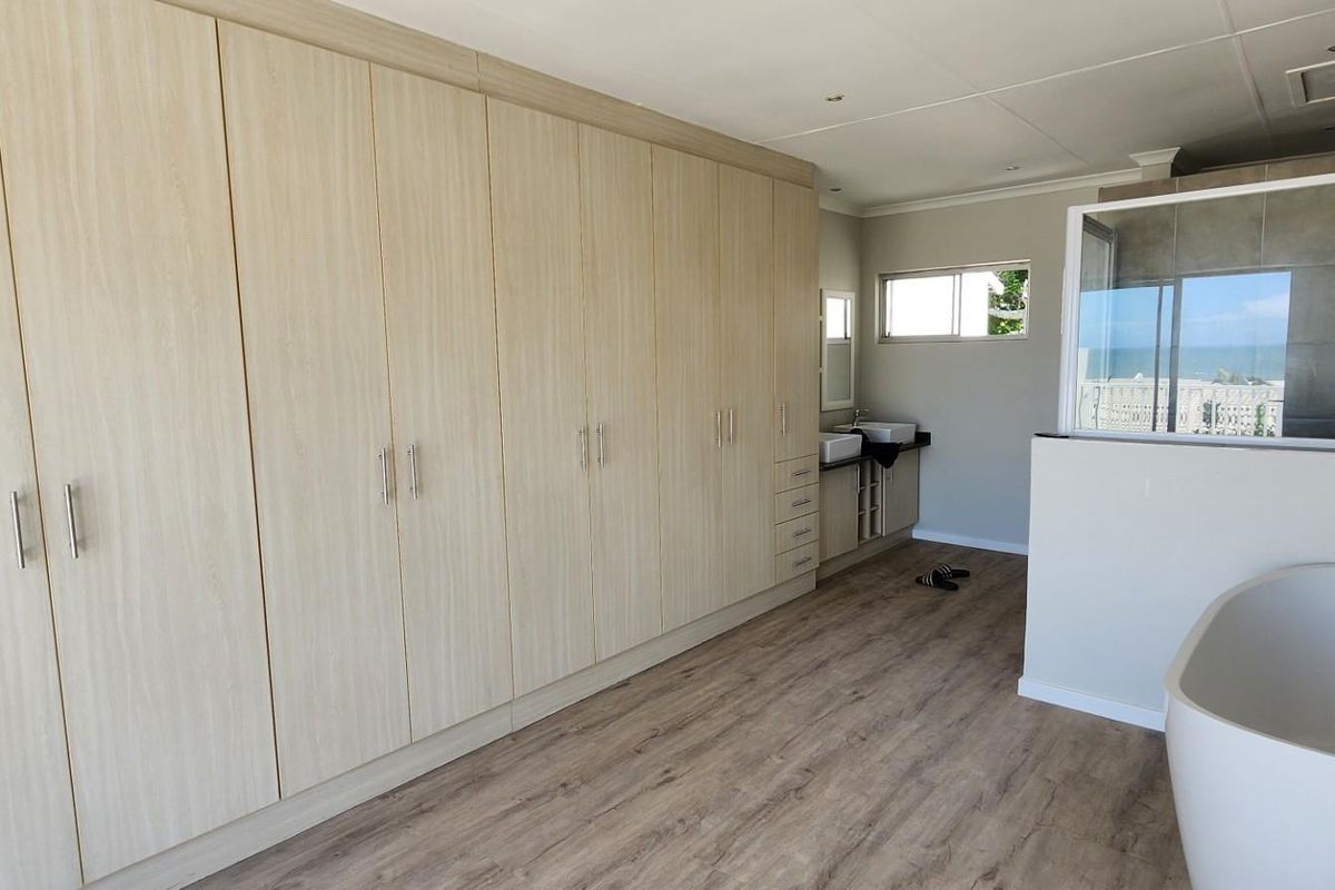 Spacious bedroom featuring extensive built-in cabinetry, an open-plan en-suite bathroom with a freestanding bathtub, glass-enclosed shower, and dual vanity basins.