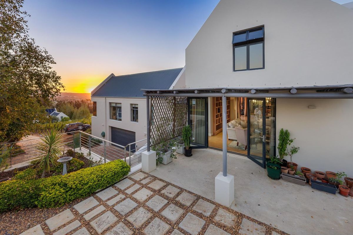 A rear patio area featuring a pergola, paved flooring, and direct access to the living space, overlooking a landscaped garden and sunset view.