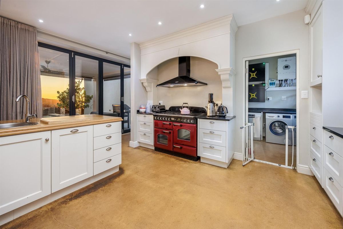 Spacious kitchen featuring a red range cooker with extractor hood, wooden countertops, and an adjoining scullery with integrated laundry and solar power system.