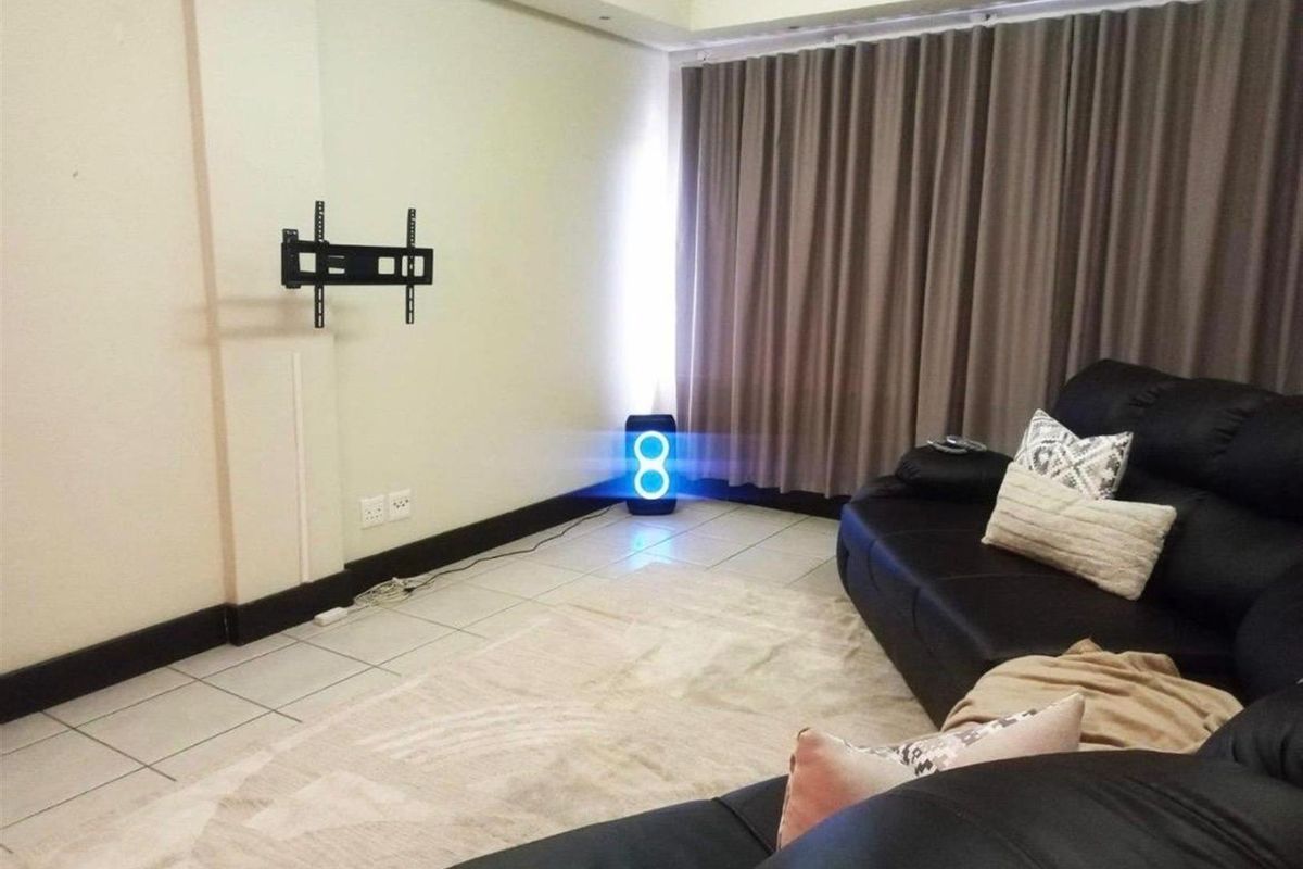 A living room featuring tiled flooring, a recessed ceiling detail, and a wall-mounted TV bracket, providing a functional space for relaxation.