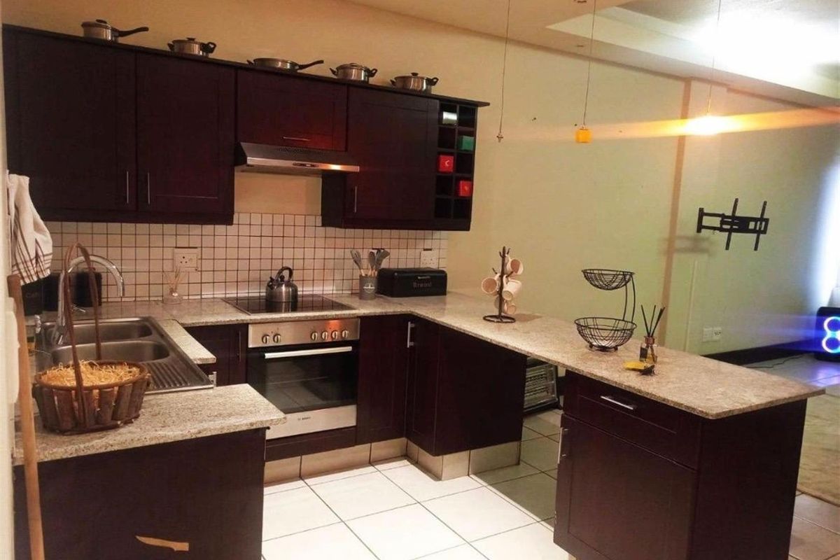 A functional kitchen featuring dark wood cabinetry, granite countertops, a built-in oven with hob, and a breakfast bar, finished with tiled flooring and backsplash.