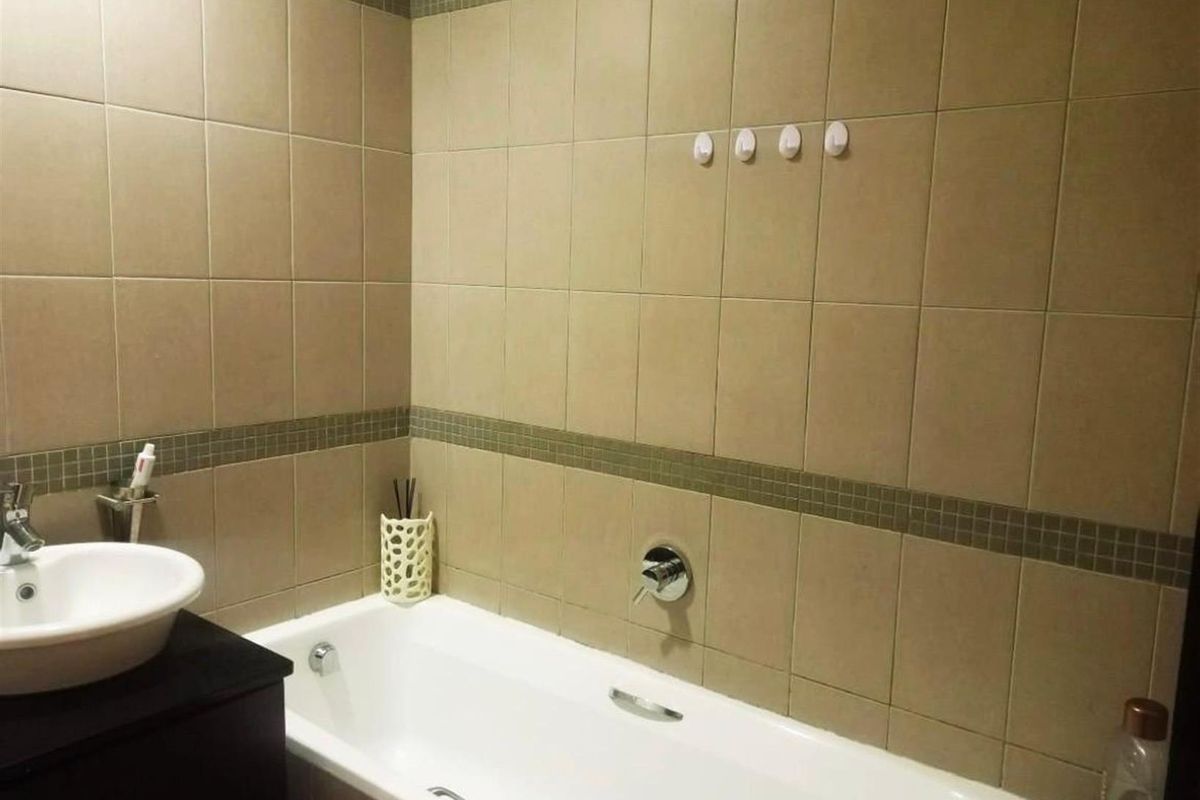 A functional bathroom featuring a bathtub with wall-mounted mixer tap, a vanity basin, and neutral wall tiling with a decorative mosaic border.