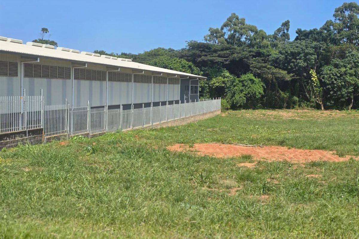 A view of the agricultural land featuring a large industrial-style structure with metal cladding and secure perimeter fencing.