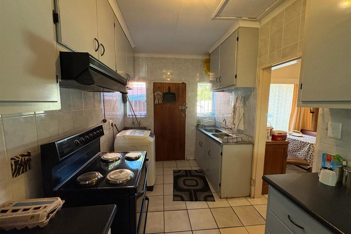 A functional kitchen featuring built-in cabinetry, a freestanding electric stove with extractor fan, double sink, and tiled flooring with direct exterior access.