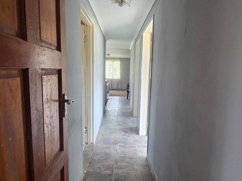 A narrow interior hallway featuring tiled flooring and multiple doorways leading to adjacent rooms, with plain grey painted walls.