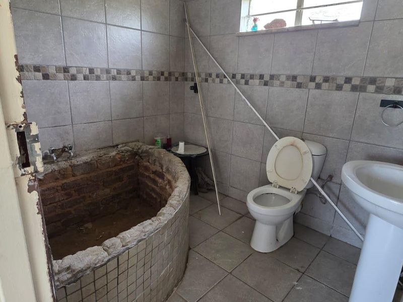 A dated bathroom featuring a custom built-in brick bathtub, pedestal basin, and toilet, requiring significant renovation and repair to finishes and plumbing.