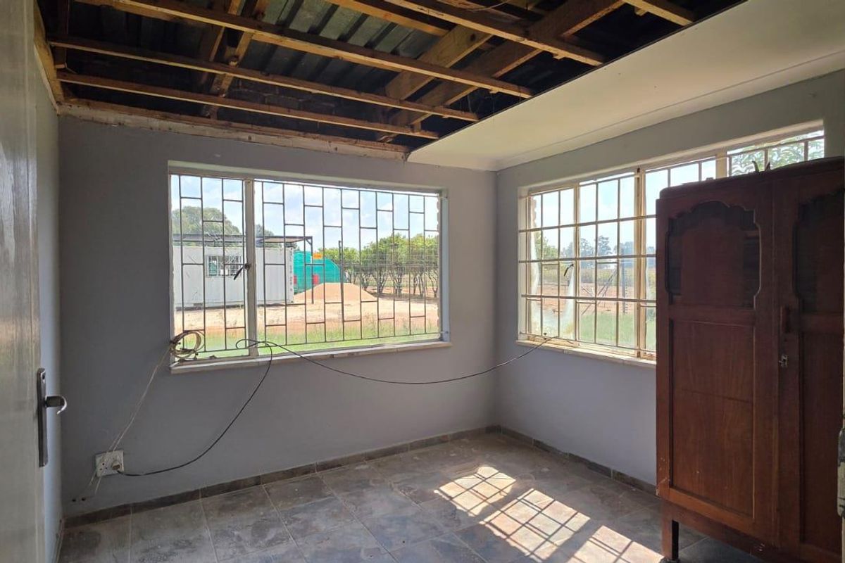 A bedroom in need of renovation, featuring tiled floors, security bars on windows, and an unfinished ceiling with exposed joists.