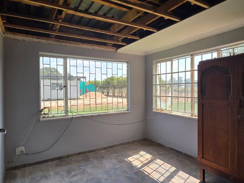 A bedroom in need of renovation, featuring tiled floors, security bars on windows, and an unfinished ceiling with exposed joists.