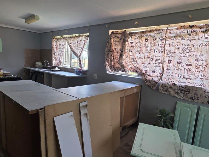 A kitchen space currently undergoing renovation, featuring exposed cabinetry carcasses, a sink, and tiled splashbacks, requiring completion of finishes and fixtures.
