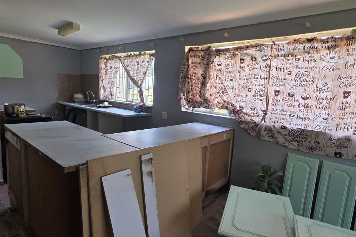 A kitchen space currently undergoing renovation, featuring exposed cabinetry carcasses, a sink, and tiled splashbacks, requiring completion of finishes and fixtures.