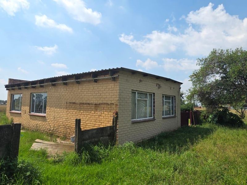 A rear view of a face brick farm building featuring steel frame windows with security bars, set within a large, grassed rural property.