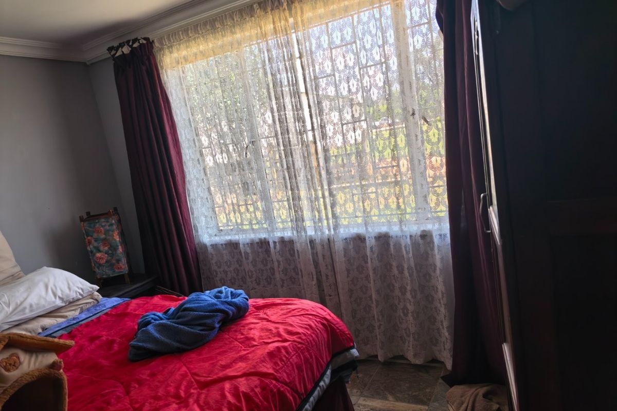A bedroom featuring tiled flooring, decorative cornice, and a window fitted with security bars.