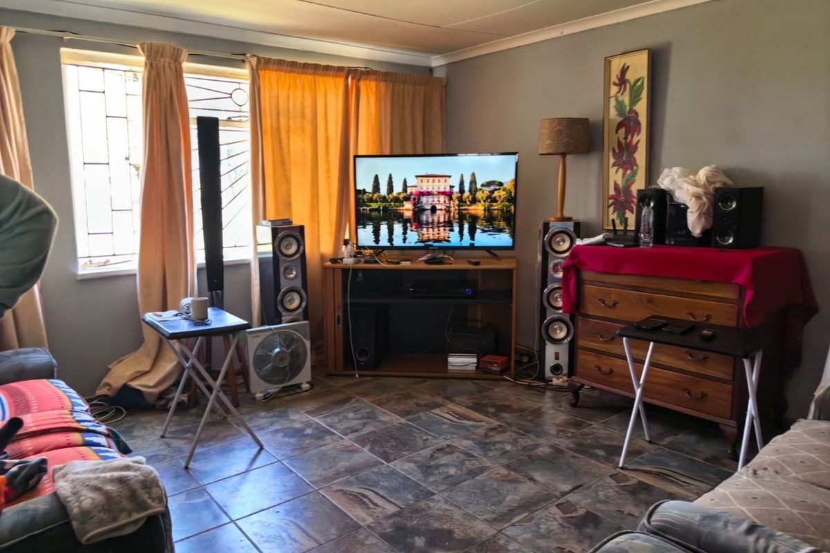 A living room featuring tiled flooring and security bars on the windows, showing signs of wear and requiring cosmetic updates.