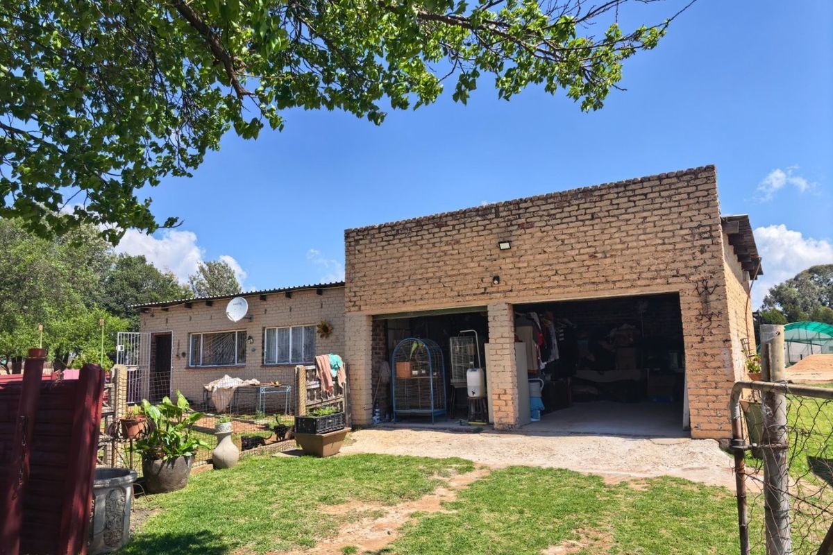 Rear view of a farm property featuring an exposed brick facade, a double garage, and a surrounding garden area with wire fencing.