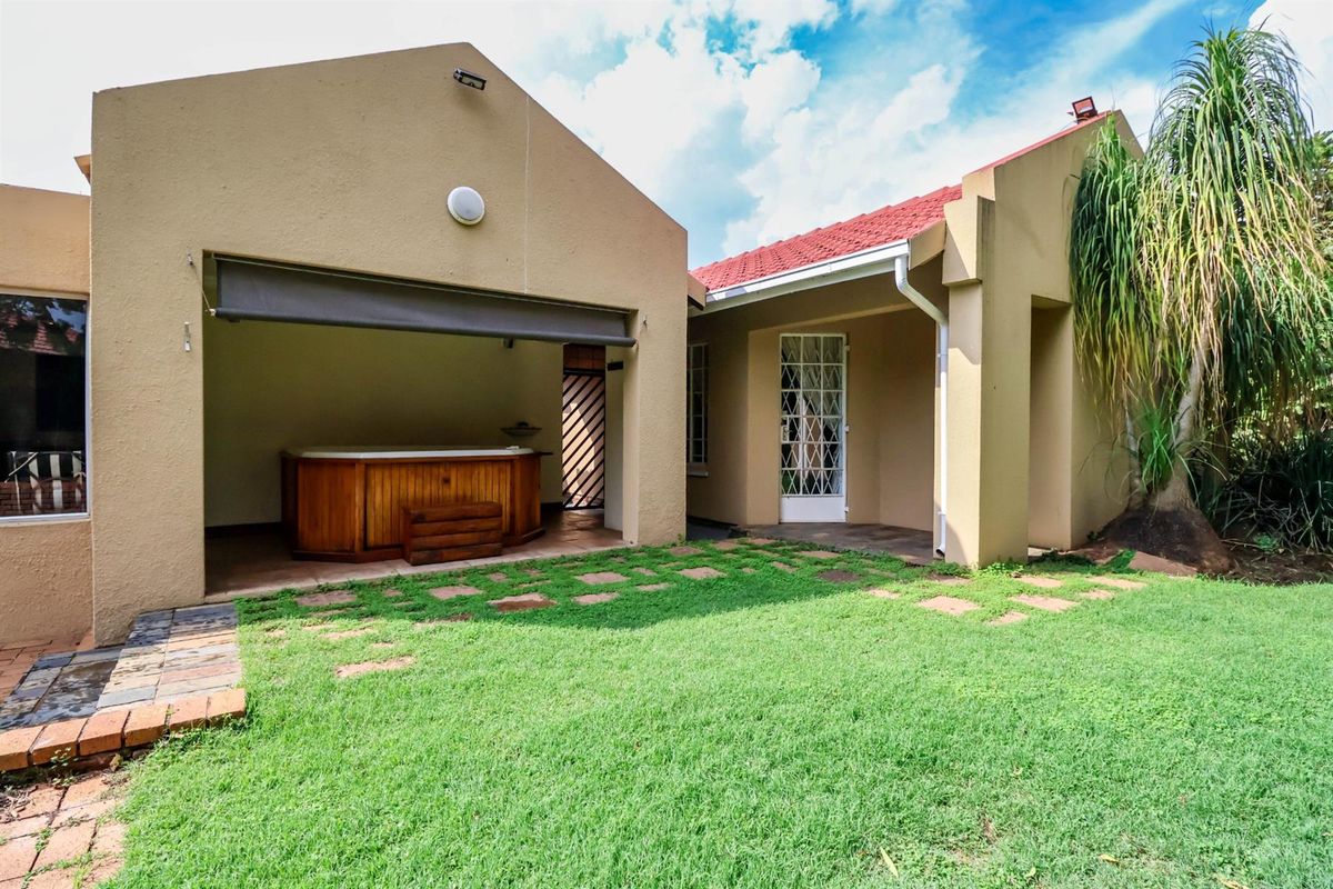 Rear view of the property featuring a covered patio area with a built-in hot tub, tiled flooring, and a landscaped garden.