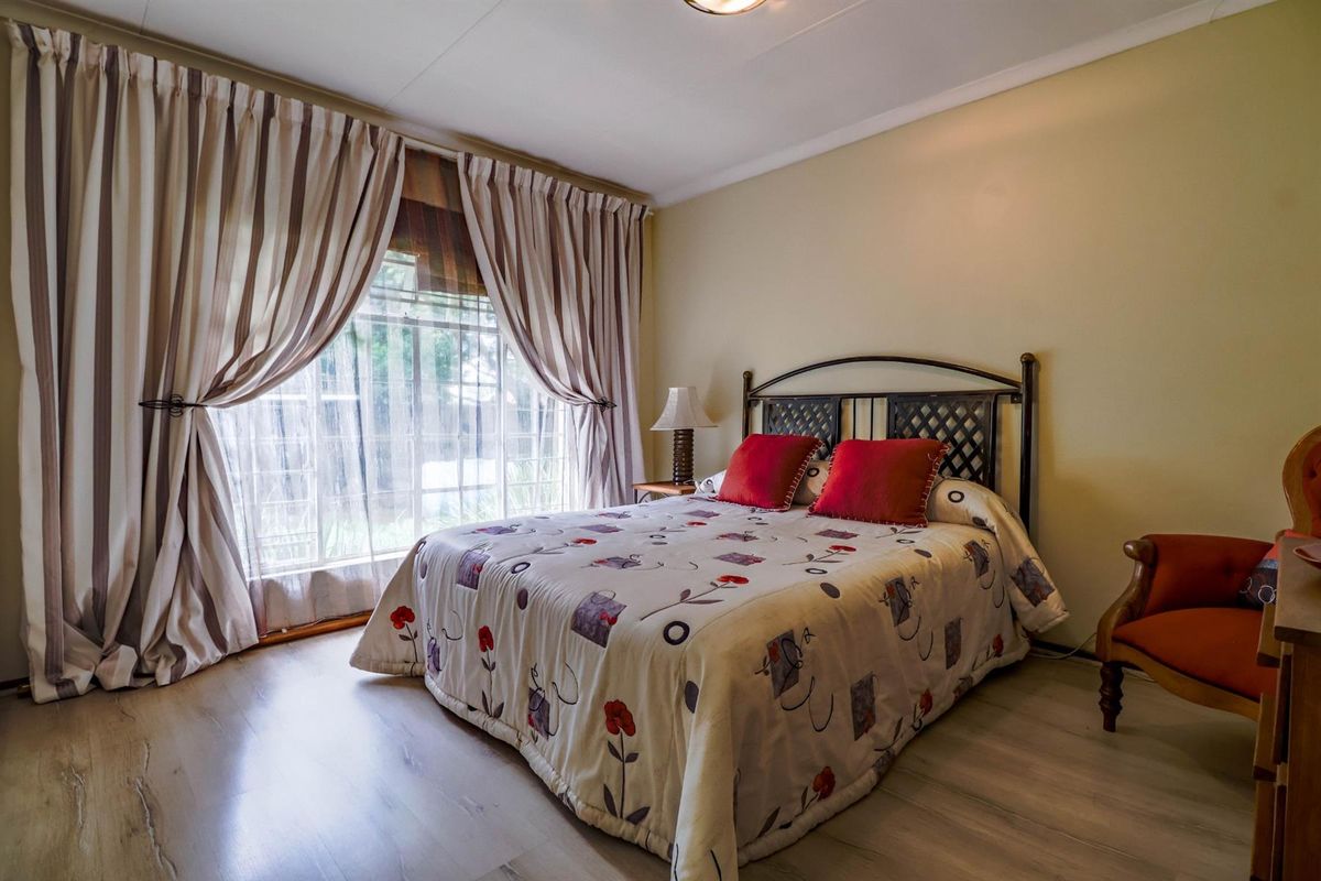 A well-lit bedroom featuring light-toned laminate flooring, neutral wall finishes, and large windows dressed with floor-to-ceiling curtains.