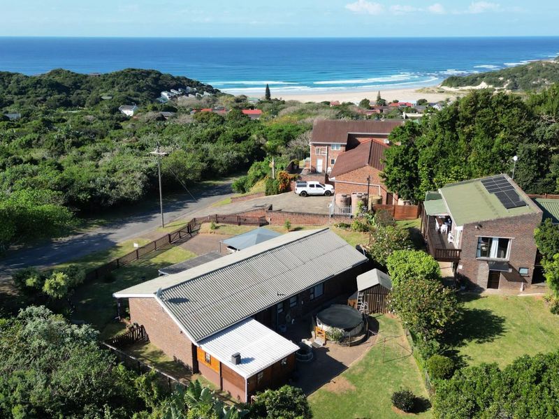 Aerial view of the property showing the main dwelling, surrounding garden, and proximity to the coastline and beach.