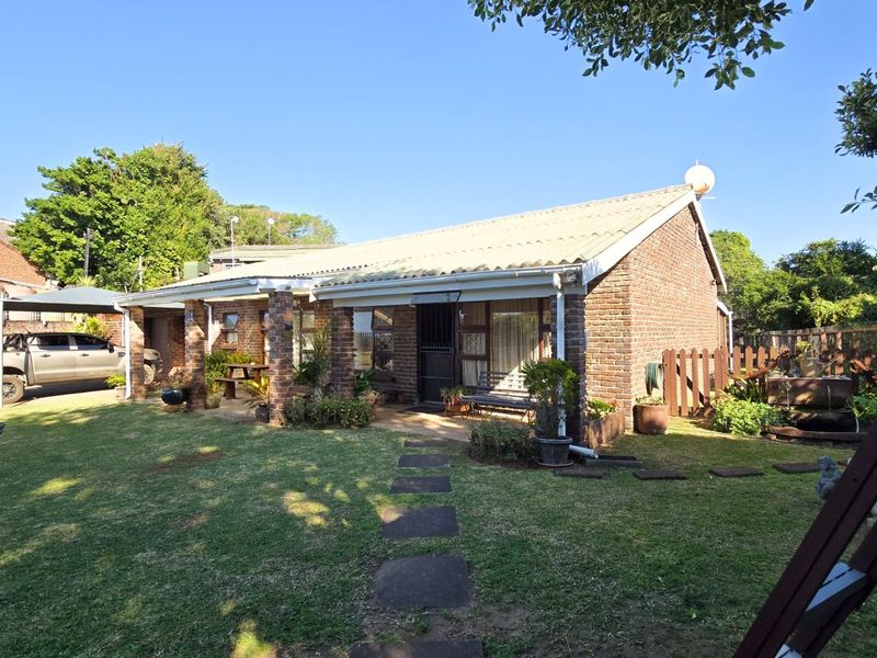A rear view of a brick-built house featuring a covered patio area, established lawn, and paved garden path.