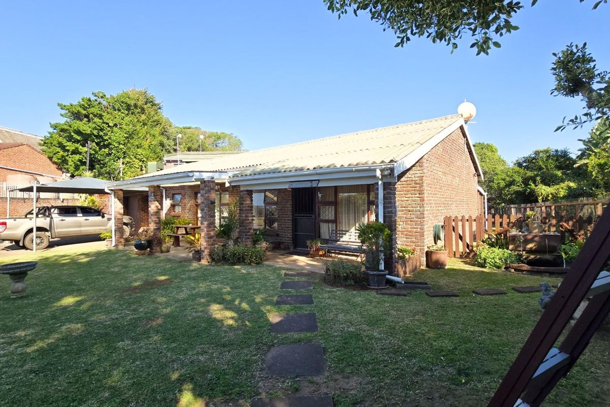 A rear view of a brick-built house featuring a covered patio area, established lawn, and paved garden path.